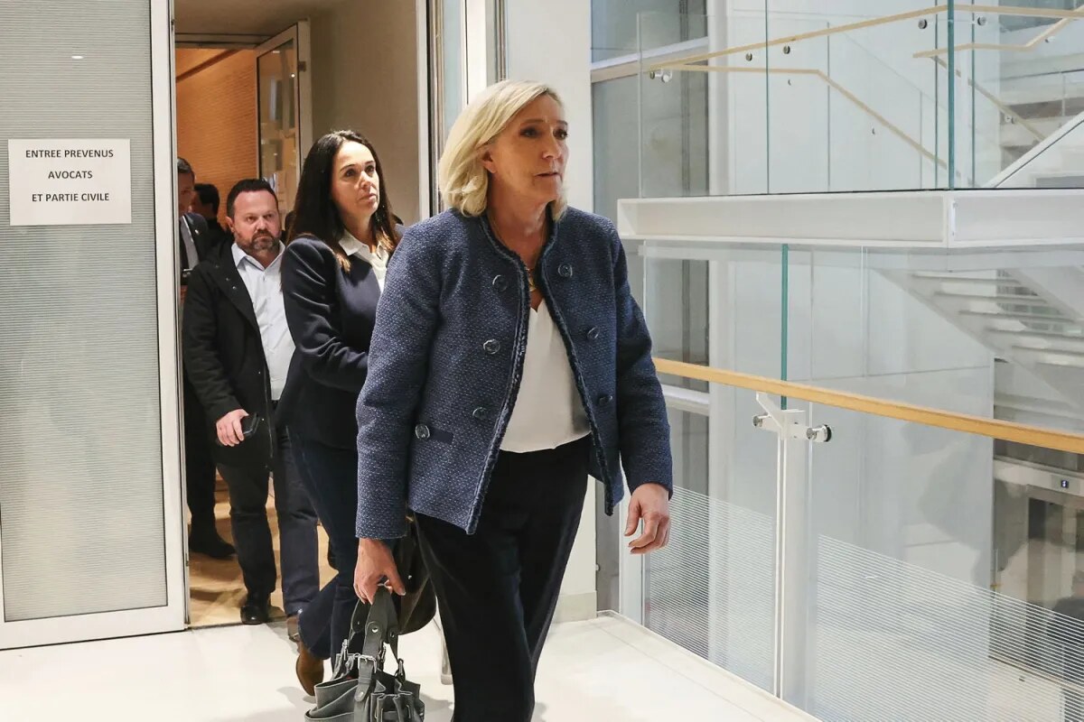 Marine Le Pen marchant dans le couloir d’un tribunal, accompagnée de plusieurs personnes.